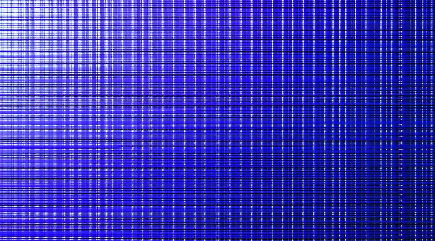 Extreme close-up of a semiconductor wafer surface with UV-lit inspection lighting showing die grid pattern